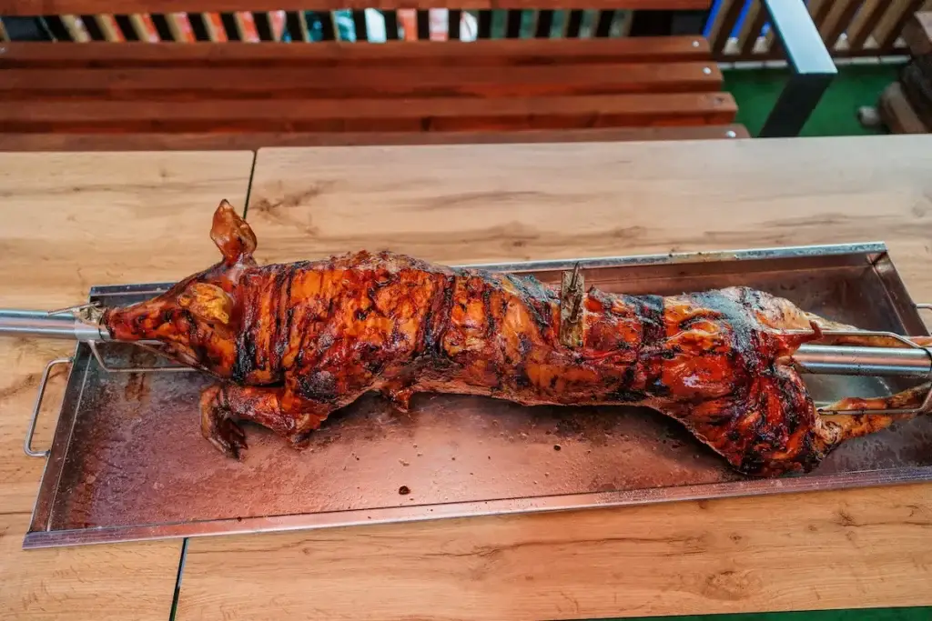 Perfectly roasted whole pig on a rotisserie with crispy skin and an internal temperature nearing ideal pull-apart tenderness.